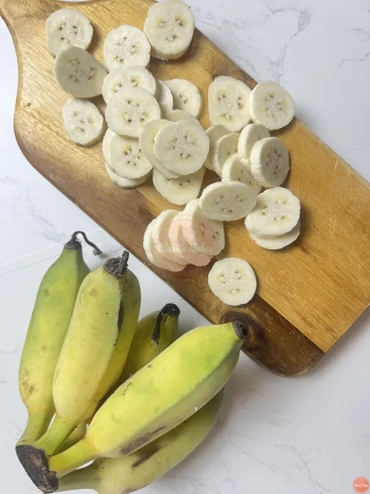 A bunch of unriped bananas placed next to a cutting board with sliced unriped bananas on top of it.