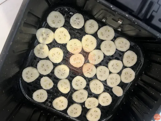 Unriped banana sliced placed inside air fryer and coated with non stick spray.