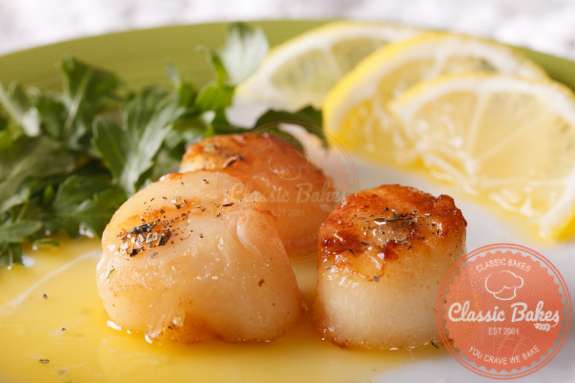 Close up shot of Garlic Butter Scallops in a plate with lemon slices and garnish