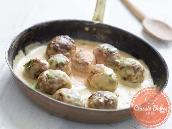 Front shot of Keto Swedish Meatballs in a skillet with wooden spatula on the side
