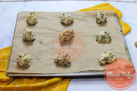 9 balls of cookie dough spread out on a baking sheet lined with parchment paper 