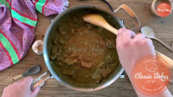 Areal view of curry goat being stirred with a wooden spoon in a pot