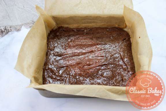 Baking pan lined with parchment paper filled with chocolate brownie batter 