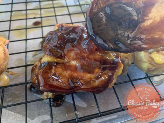 Chicken on a cooling rack with dark sauce being added to the chicken 
