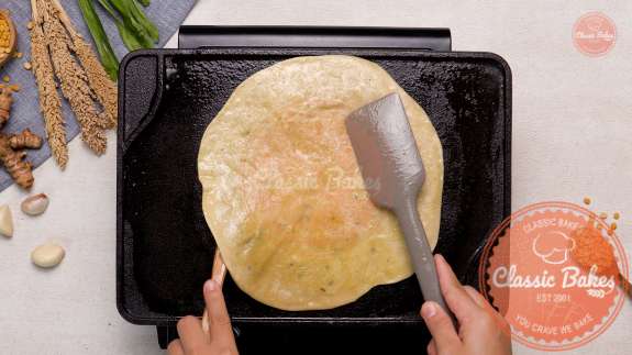 Dhal Puri cooking on a tawa with a spatula underneath it 