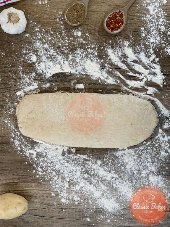 Dough rolled out on a countertop into a rectangular shape with flour sprinkled around it. 