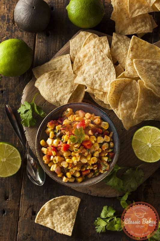 Aerial shot of Grilled Corn Salsa in a bowl with nachos and tortillas on the side