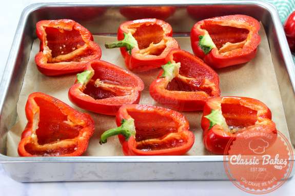 Overview of a baking sheet lined with parchment paper containing red peppers cut in half 