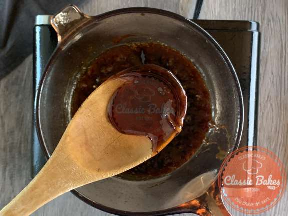 A pot with dark colored sauce being stirred with a wooden spoon 