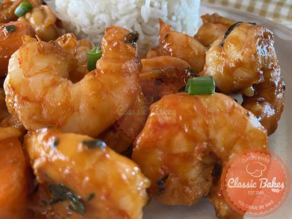 Shrimp and vegetables tossed with red sauce on a plate with white rice 