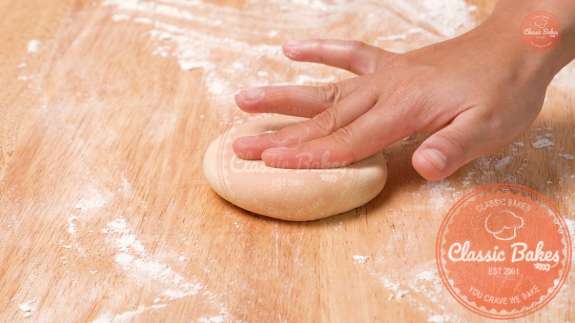 Stuffed dough on a floured surface being flattened by hand 