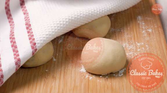 Stuffed dough resting on a floured countertop with a kitchen towel covering them 