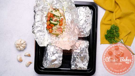 Arial view of a baking sheet with four tilapia foil packages with one package unwrapped