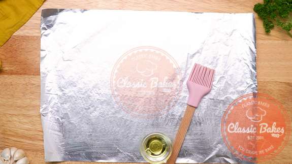 Arial view of a sheet of foil being brushed with olive oil using a pastry brush