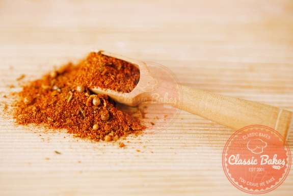 BBQ chicken rub spices in a spoon on a wooden countertop 