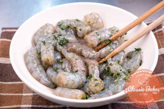 A bowl of shrimp being tossed in green seasoning with chopsticks 
