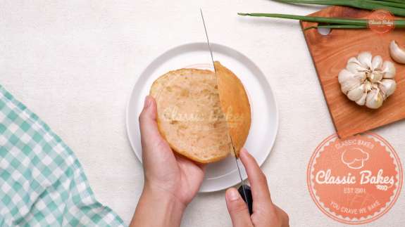 Bun being cut with a knife in half on a plate 