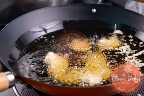 Chicken tempura batter being fried in a pot of oil 