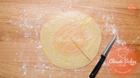 Circle of dough on a floured countertop being cut with a pairing knife 