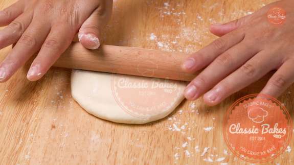 Dough being rolled out with a rolling pin on a countertop 