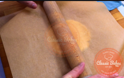 Dough being rolled with a rolling pin between two pieces of parchement paper