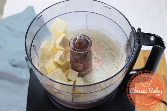 Food processor containing dry ingredients and cubes of vegan butter