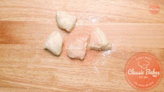 Four pieces of cut dough on a floured countertop 