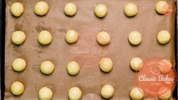 Overview of a lined baking sheet with 24 small balls of dough resting 