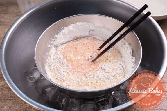 Overview of tempura batter being mixed with chopsticks in a bowl over ice 