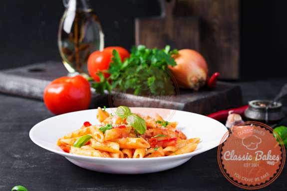 Sideview of a bowl of pasta arrabiata with ingredients in the background 