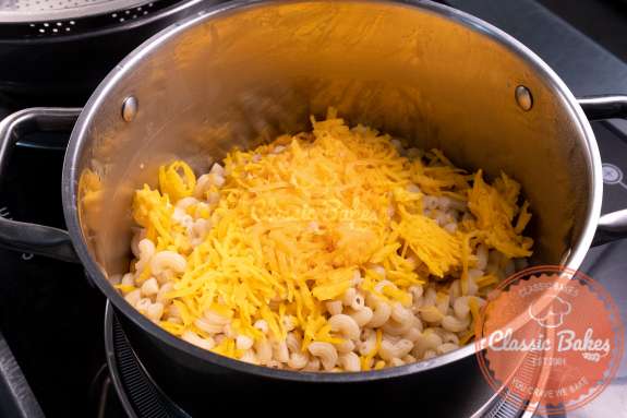 A pot containing cooked macaroni with shredded cheese on top 