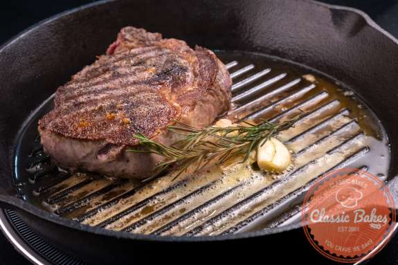 Ribeye steak in a pan with butter rosemary and cloves of garlic 