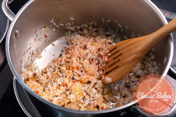 Rice being stirred with a wooden spoon in a pot with beans and vegetables 