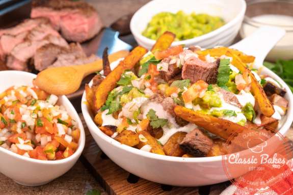 Sideview of a bowl of carne asada with guacamole steak and Pico de Gallo in the background 