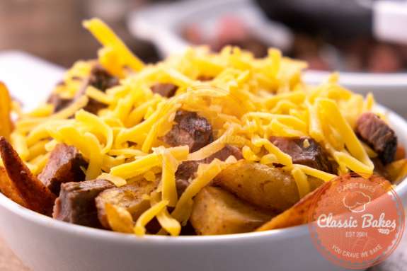 Sideview of fries with shredded cheese and pieces of steak on top 