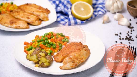 Sideview of two plates of air-fried tilapia with vegetables on the side 