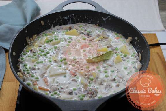Skillet containing vegetables lentils and coconut milk cooking on a gas burner 