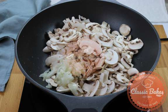 A skillet on a gas burner containing mushrooms and onions 