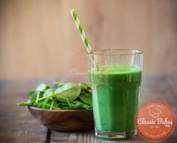 Sideview of a spinach smoothie with a wooden bowl of spinach
