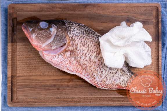 Whole snapper on a cutting board being patted dry with a paper towel 