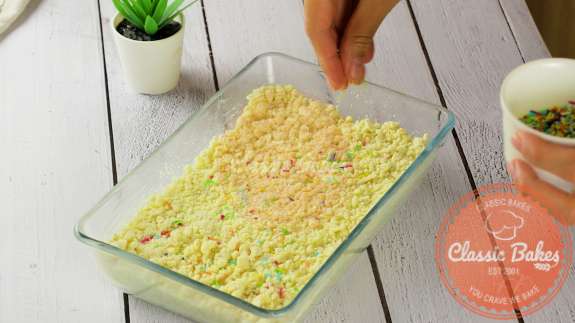Barfi ingredients pressed into a pan being topped with sprinkles 