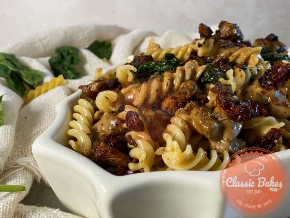 A large serving bowl of chicken spinach rotini pasta and sundried tomatoes  