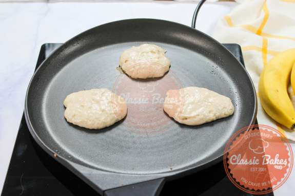 Sideview of three pancakes cooking in a skillet 