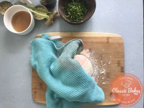 Areal view of dumpling dough on a cutting board being covered with a kitchen towel. 