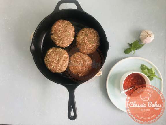 Areal view of a skillet with 4 lamb burgers cooking inside 
