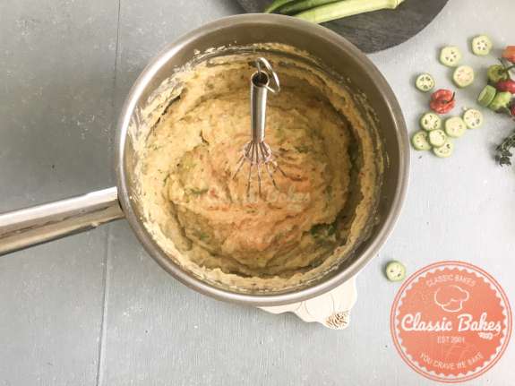 Areal view of a whisk standing up in a pot of coo coo with okra 