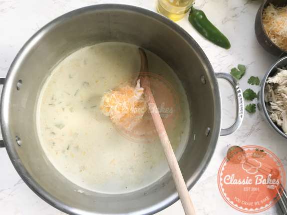 Cream cheese and shredded chicken being mixed into a pot 