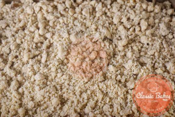Cruble topping being sprinkled on top of peach crumble bars. 
