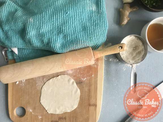 Dumpling dough being rolled with a rolling pin on a cutting board 