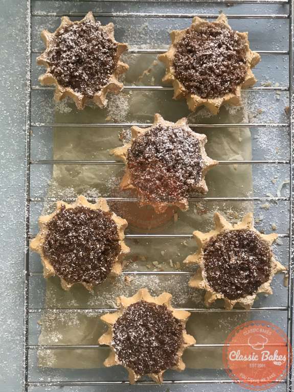 Gizzada tarts dusted with powdered sugar on a cooling rack 